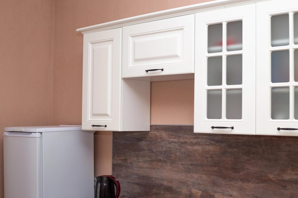 White kitchen cabinets with glass fronted upper doors beside a white refrigerator