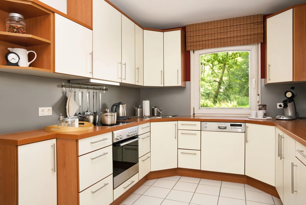 Compact L-shaped kitchen with white cabinets, a wood counter and a window above the sink