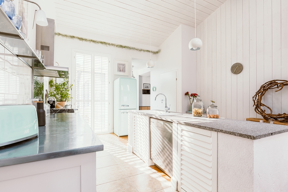 Bright white kitchen with a pale stone counter, a mint green refrigerator and a window above the sink