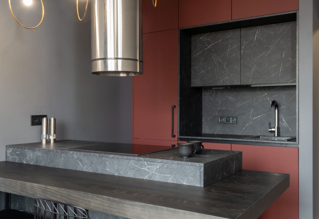 Compact kitchen island in dark stone with a stainless steel extraction hood above