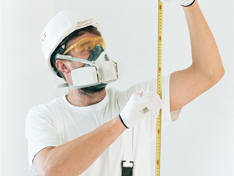 Contractor in a hard hat measuring a wall with a tape measure