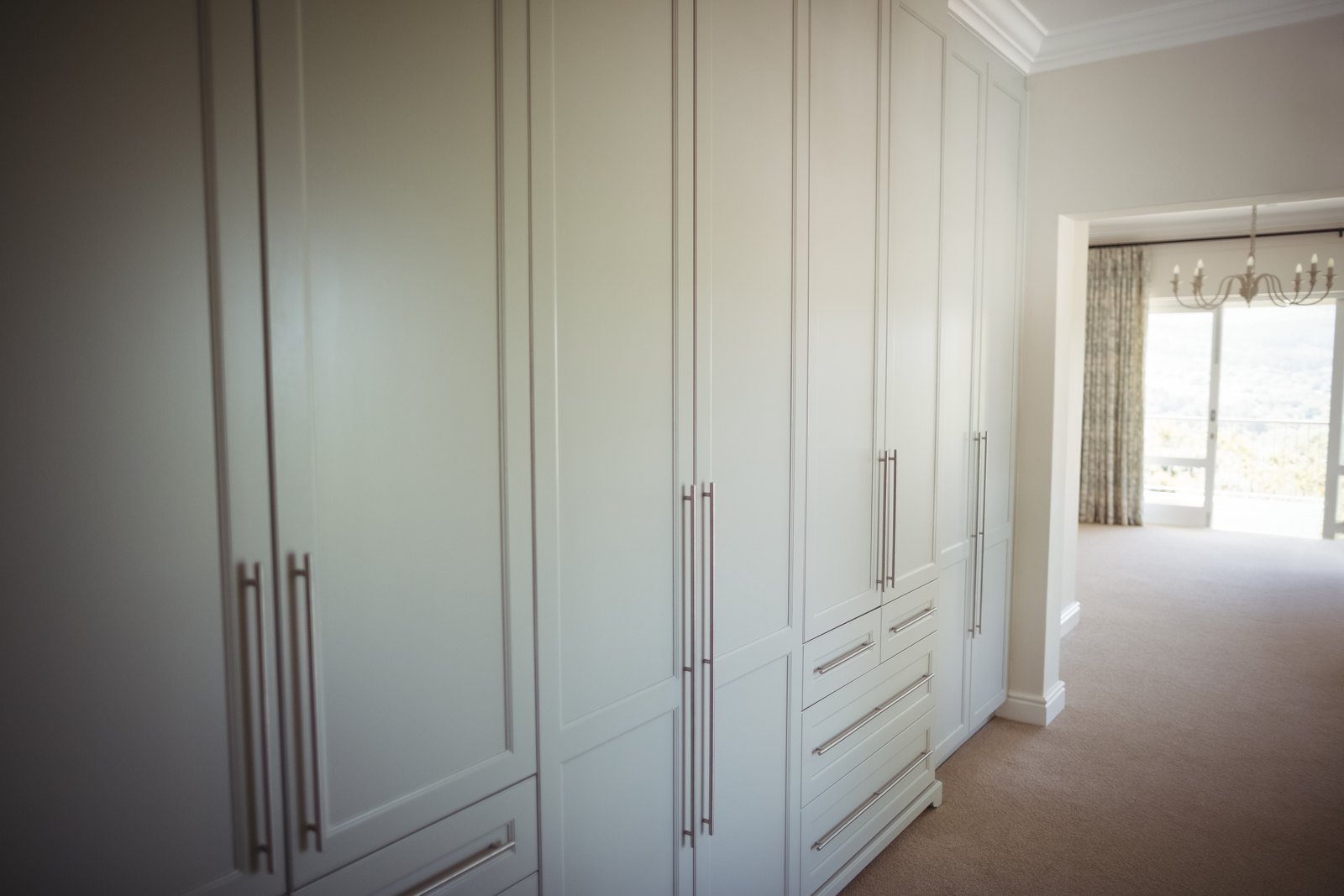Floor to ceiling built in white wardrobe with long handles and a run of drawers