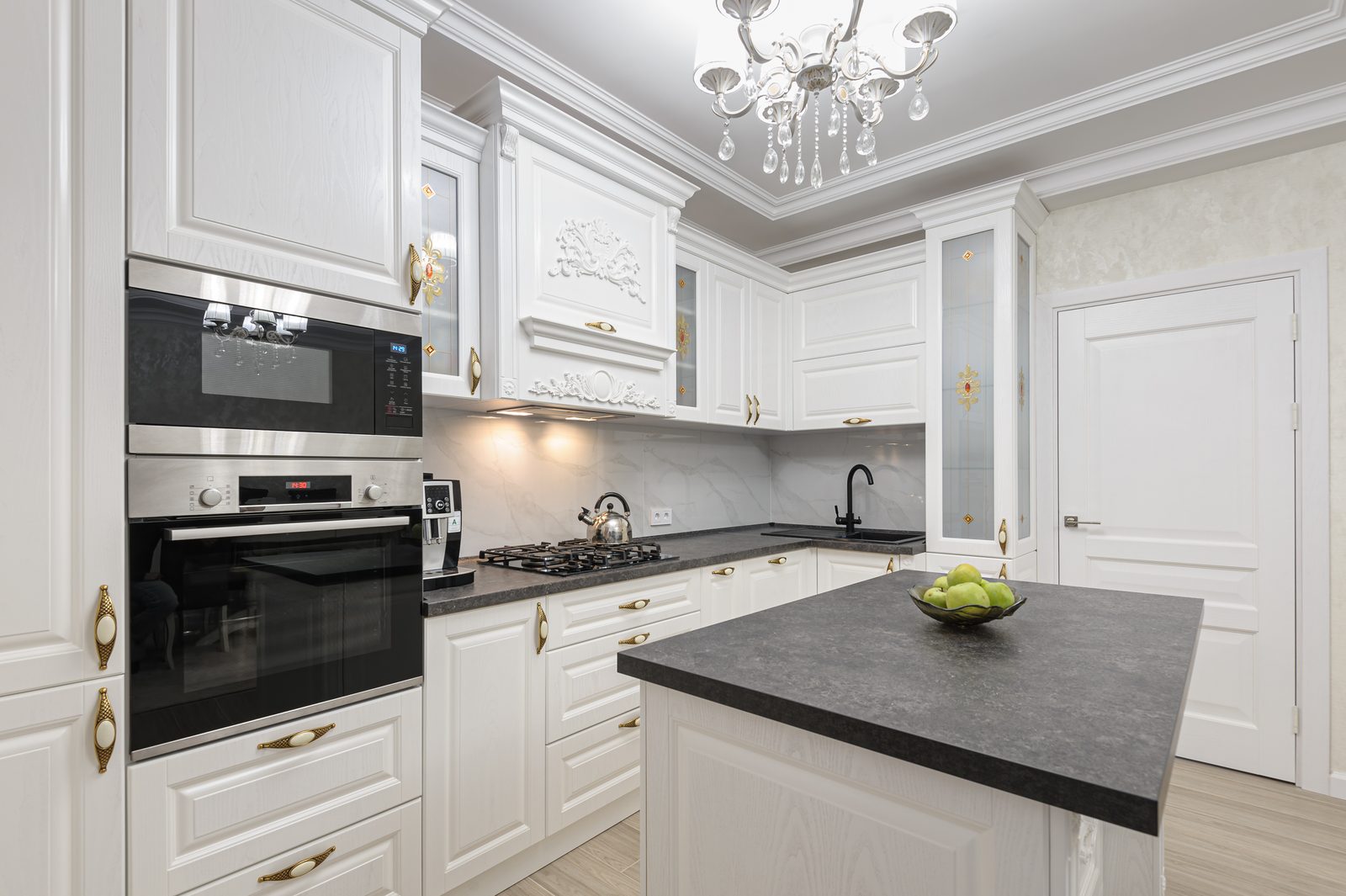 White kitchen with brass handles, a dark stone island and built in ovens