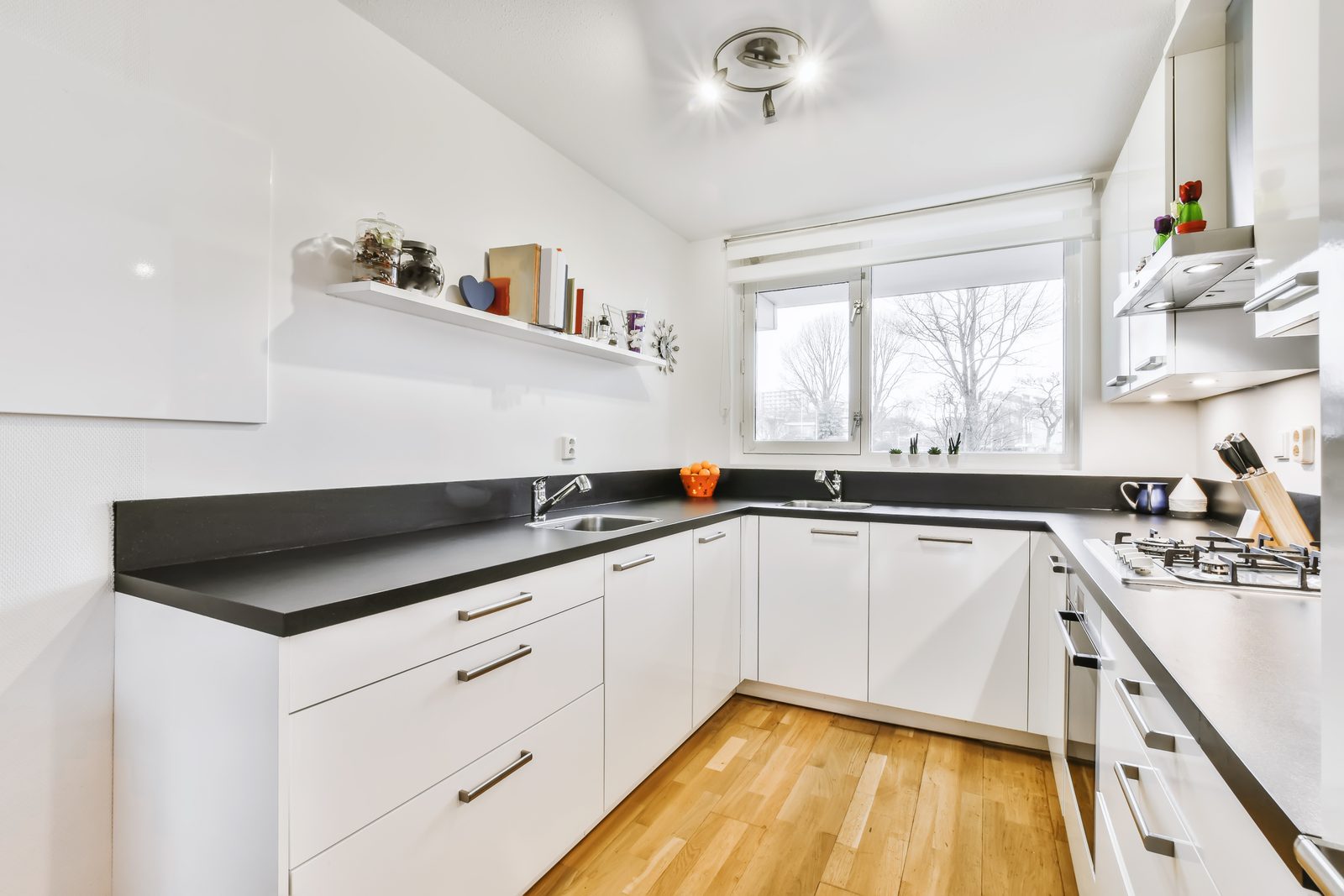 Compact white kitchen with dark counters, wood flooring and a window over the run