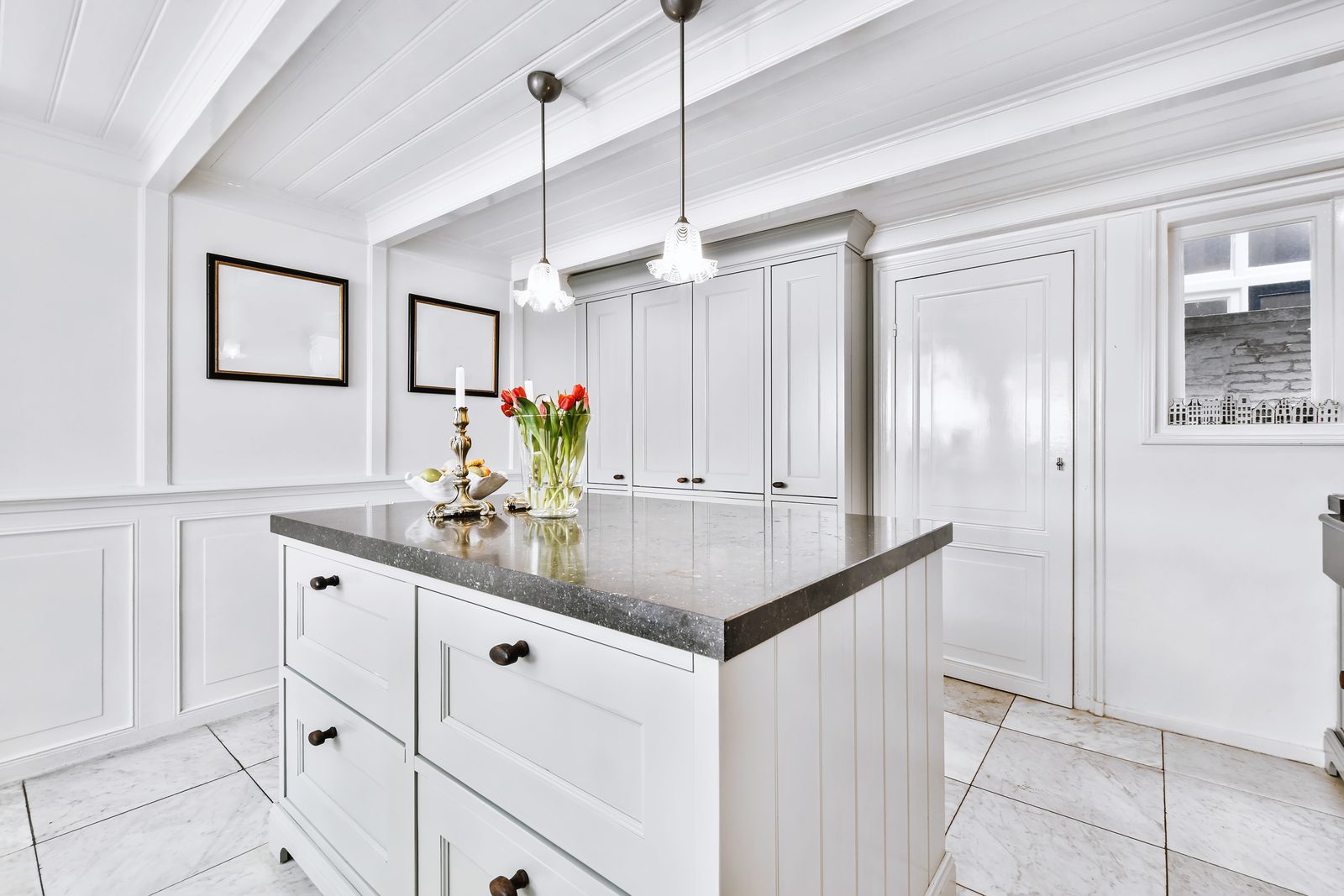 White kitchen with a dark stone island, pendant lights and a vaulted ceiling