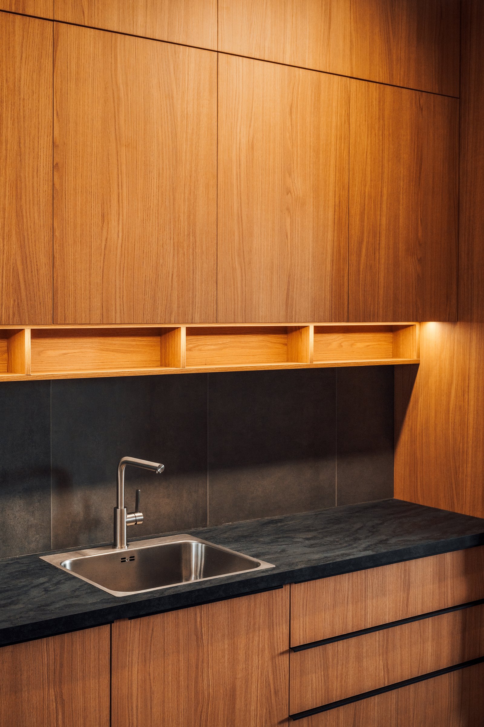 Full height timber cabinet wall with an integrated sink and a dark stone counter