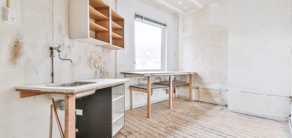 Gutted kitchen after demolition with exposed plumbing and bare walls