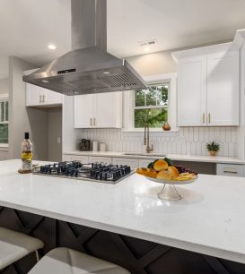 Stainless steel range hood over a gas cooktop on a white quartz kitchen island