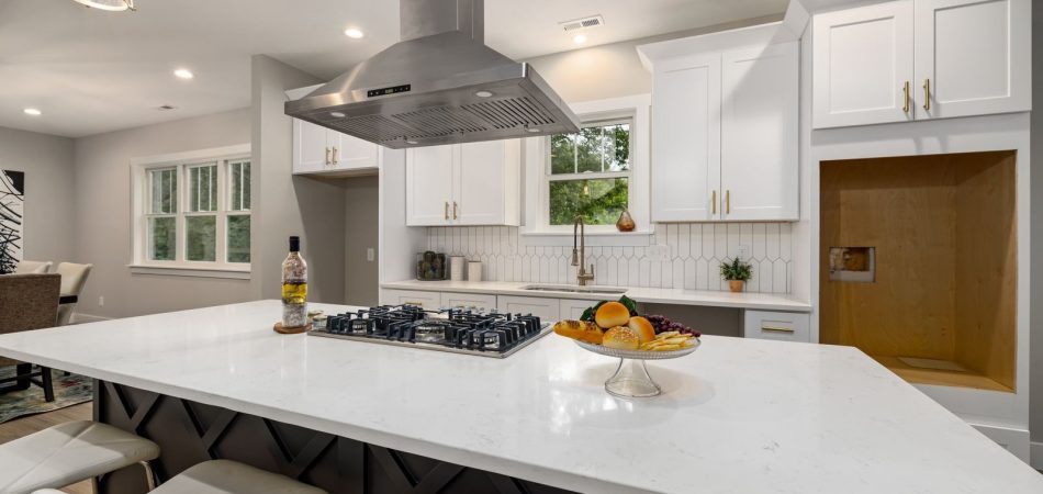Stainless steel range hood over a gas cooktop on a white quartz kitchen island